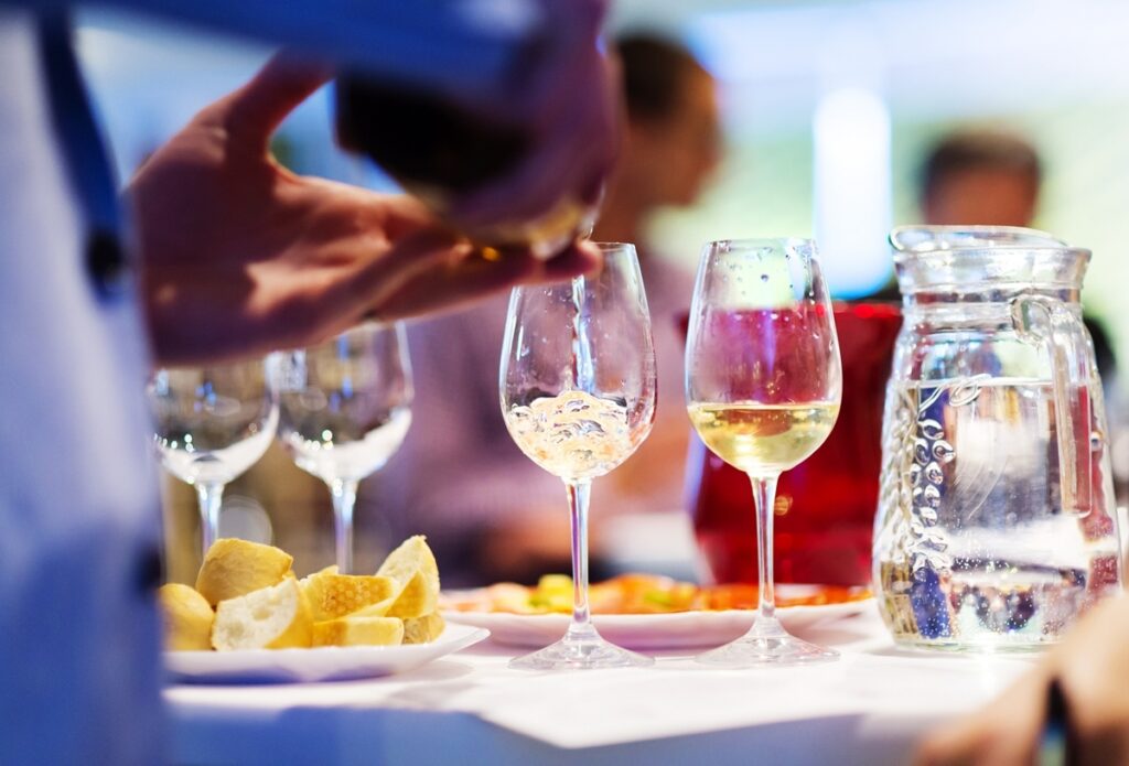 White wine being poured into a wine glass at a tabletop.